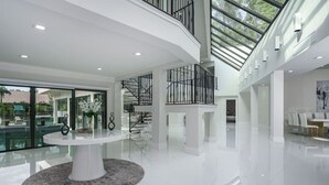 Een ruim, modern interieur met een witte tafel in het midden, een trap en een groot raam.