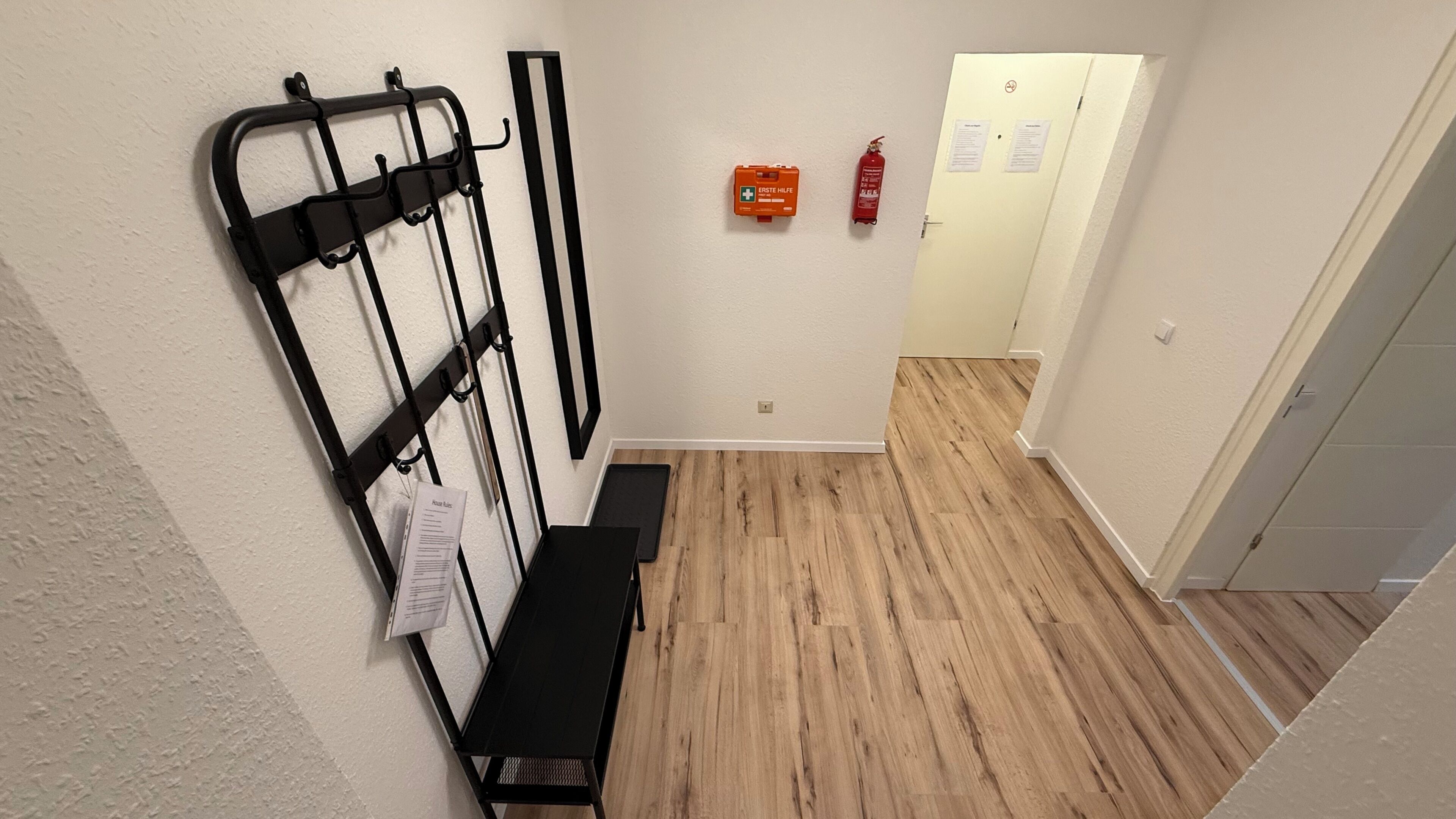 A narrow hallway with a black metal rack, a fire extinguisher, and a door with emergency instructions.