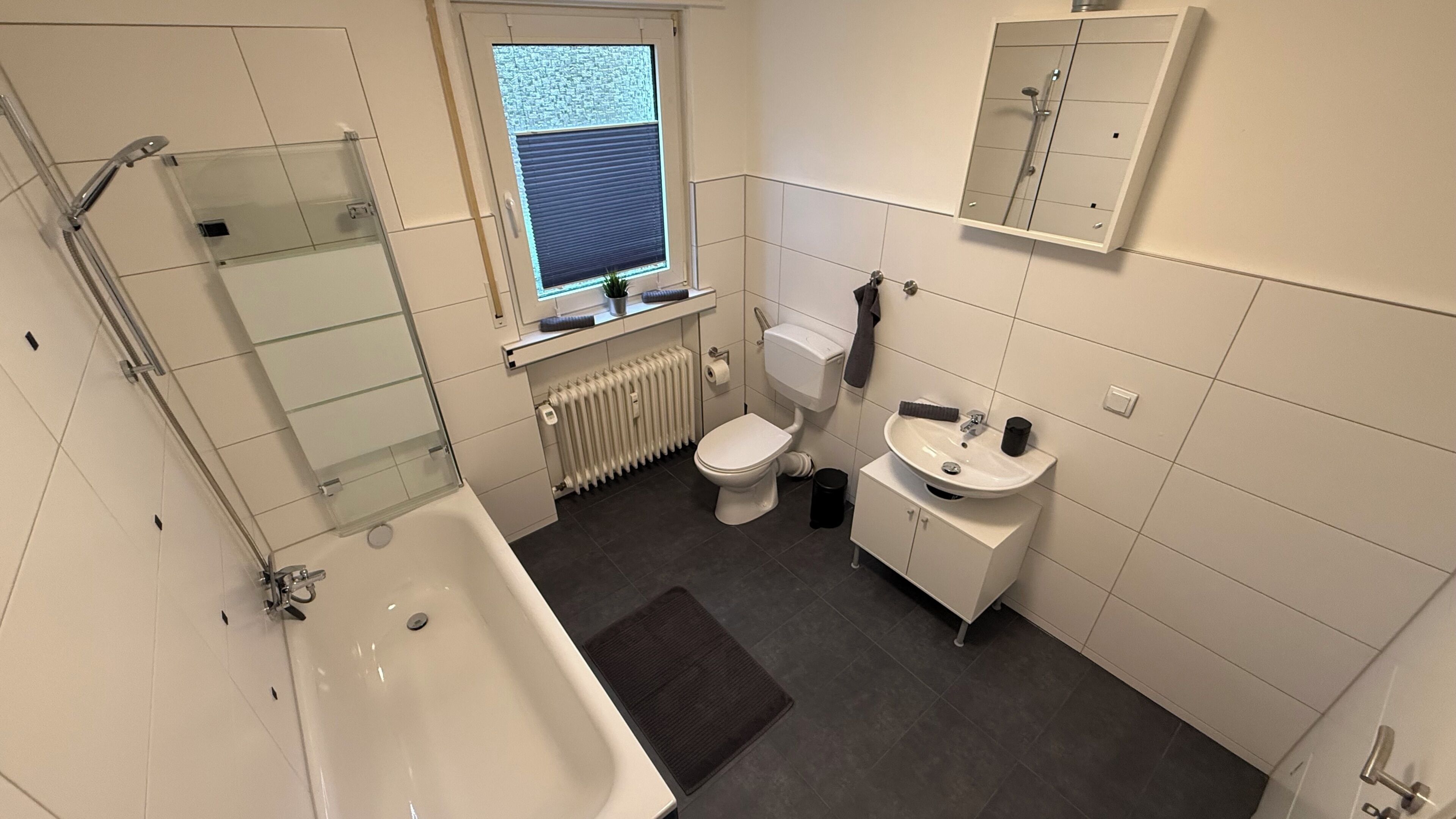 Un baño con bañera, inodoro, lavamanos y ventana con persianas.