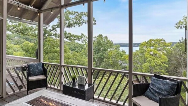 Un espace extérieur aménagé, partiellement abrité, avec un foyer, des rampes en bois et une vue sur un lac et des arbres.