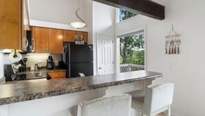 Une cuisine avec des meubles en bois, un réfrigérateur noir, un plan de travail en granit et une porte blanche donnant sur un balcon.