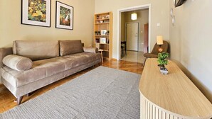 A living room with a sofa, a rug, a wooden side table with a lamp, and a bookshelf. - El Prestige Apartment - Athens Town (Athens)