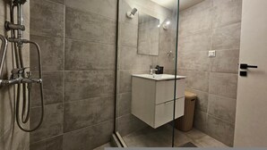 Une salle de bain moderne avec une douche à parois de verre, un meuble-lavabo blanc et une poubelle.