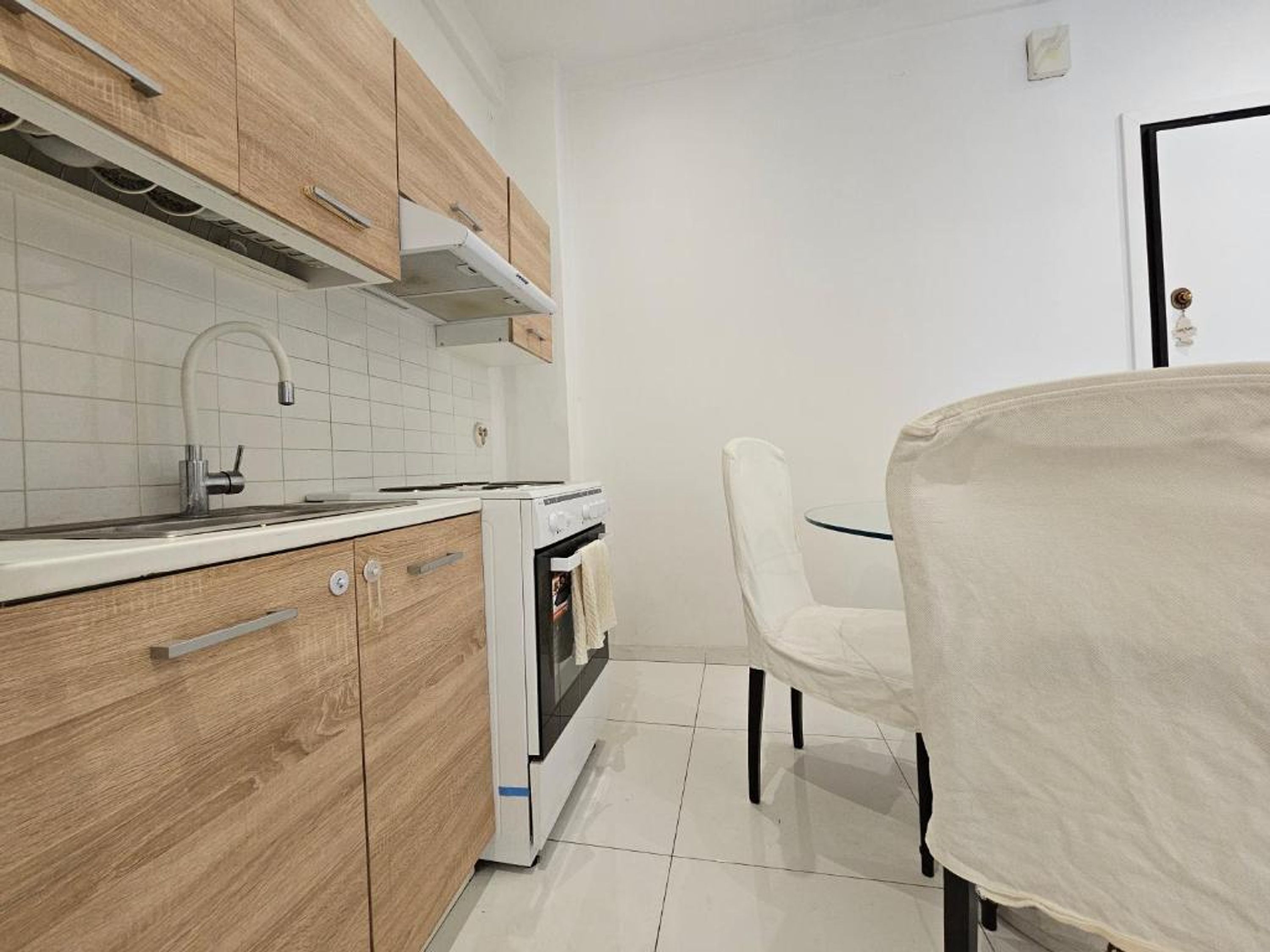 Cozinha com armários de madeira, bancada branca, fogão e um espaço de refeições com mesa e cadeiras.