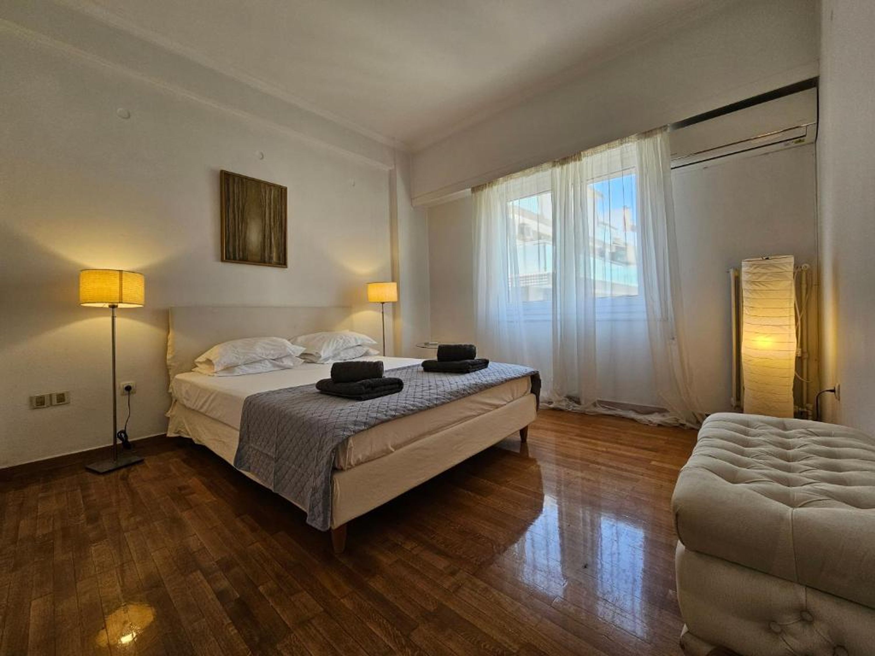 A bedroom with a bed, bedside lamps, a chair, and a window with curtains.