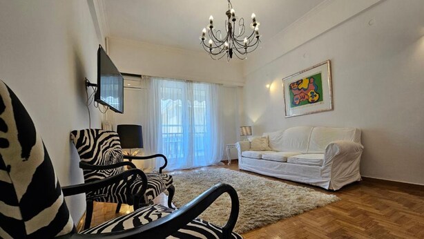 A living room with a zebra-patterned chair, a white sofa, a chandelier, and a painting on the wall. - Elegant Kifisias Experience Stay - Athens Town (Athens)