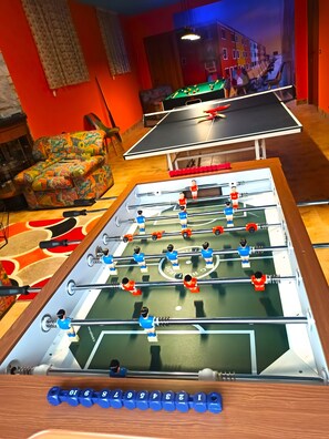 Ein Fußballtisch in einem Raum mit einer Couch und einem Tischtennistisch.