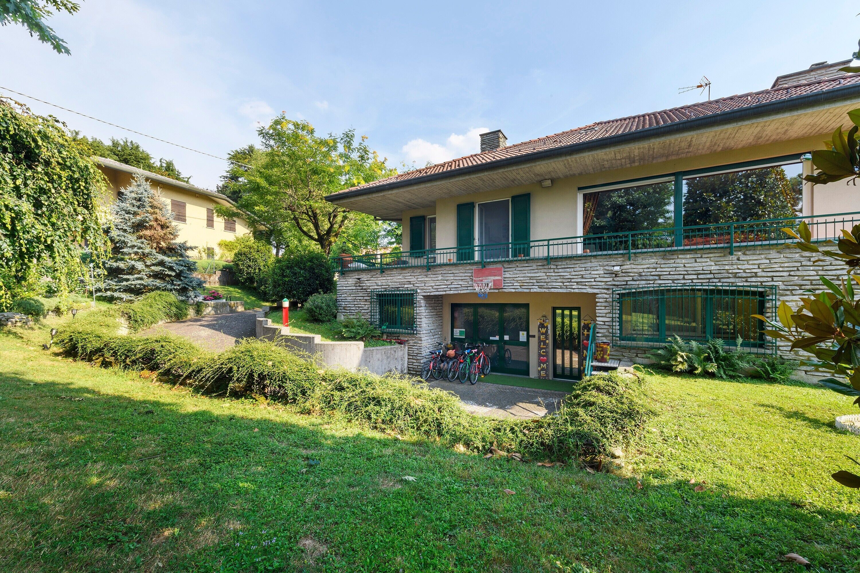 Un edificio a due piani con facciata in pietra, un balcone con ringhiere verdi e un cartello con la scritta 'WELCOME'.