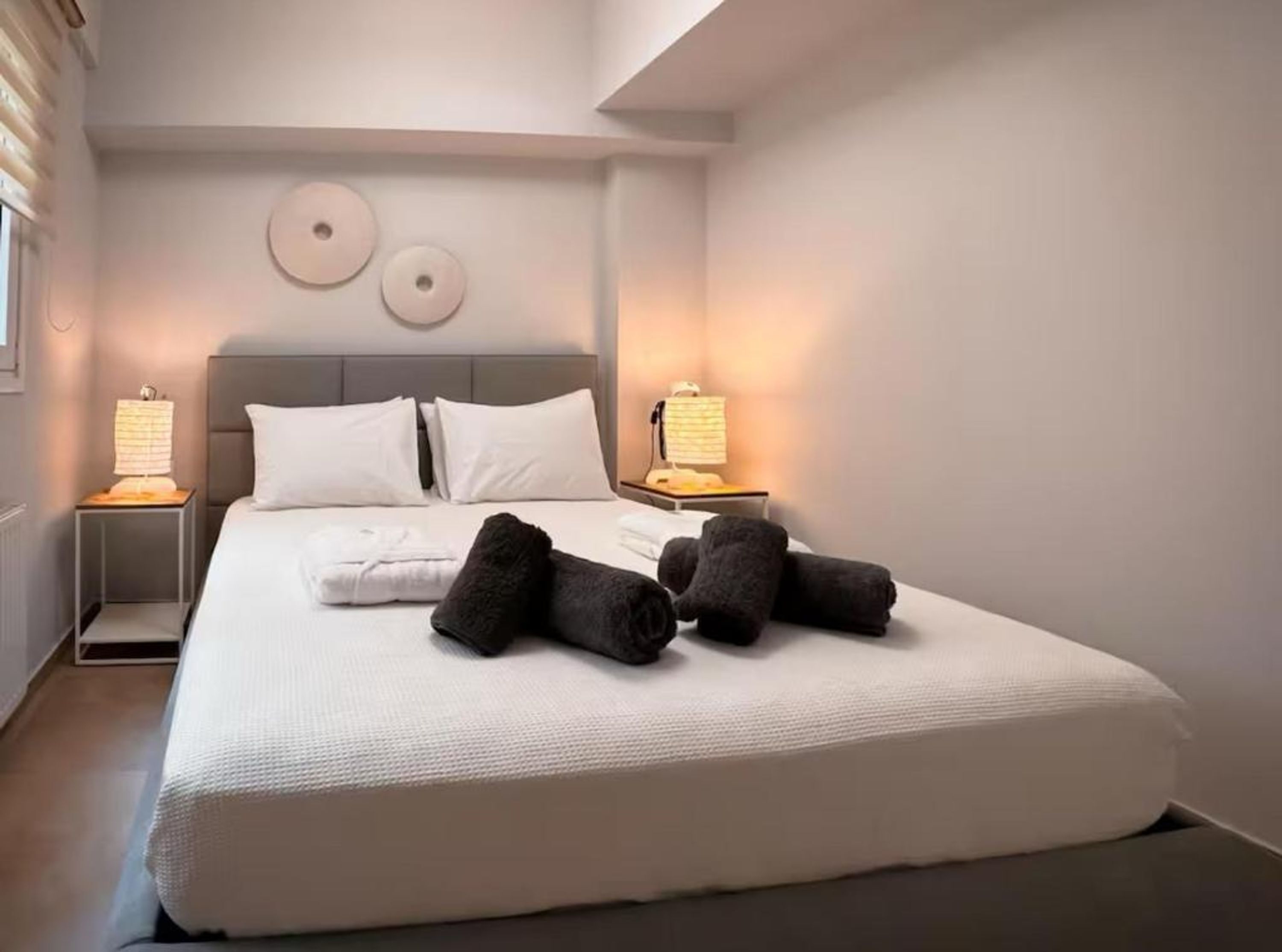 Ein ordentlich bezogenes Bett mit weißen Leinen, zwei Nachttischlampen und einem Kopfteil.