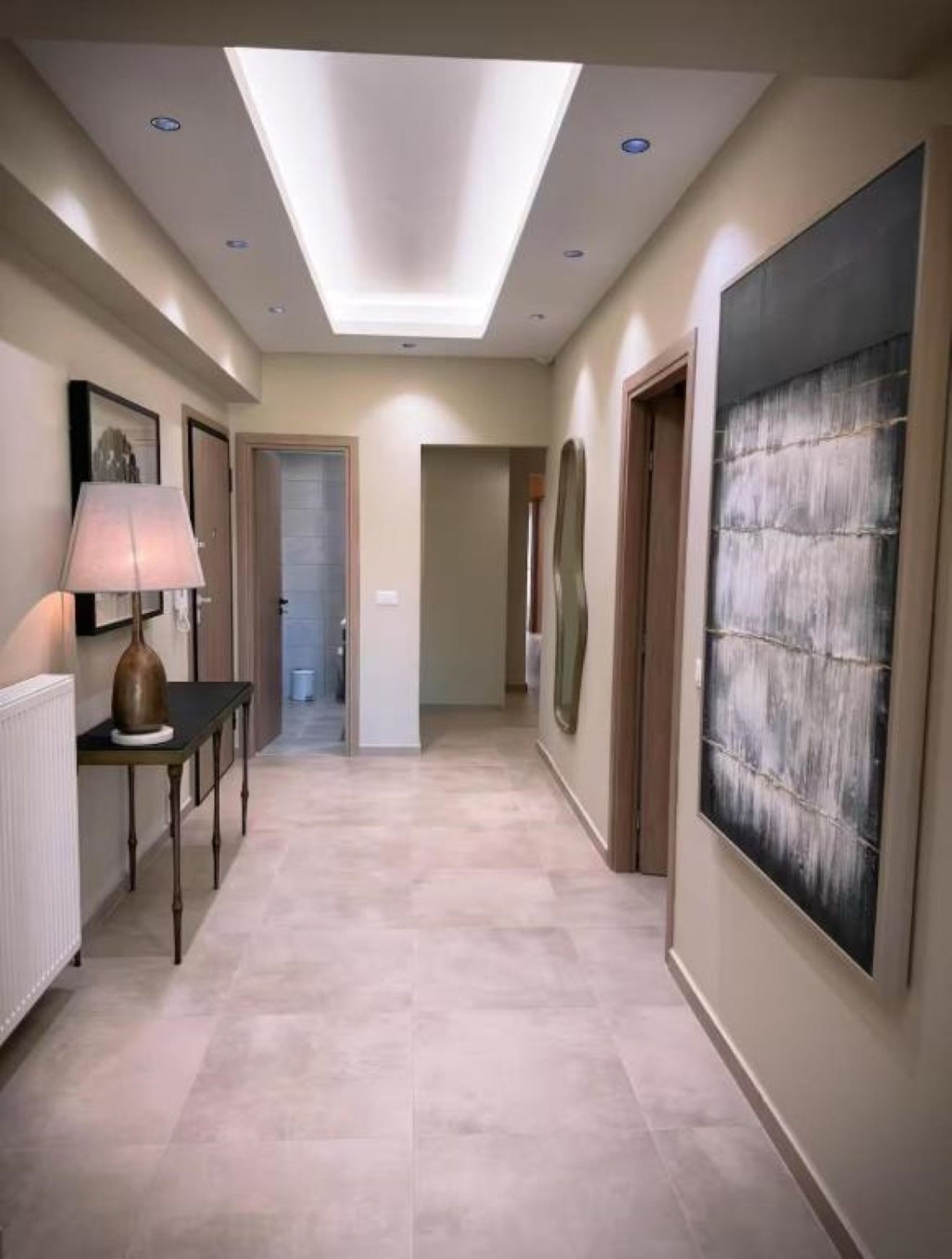 A hallway with a skylight, a table with a lamp, and a large abstract painting on the wall.