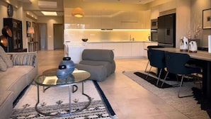 A modern living room with a sofa, a glass coffee table, and a dining area with chairs. - Elegant VIP Apartment - Athens Town (Athens)