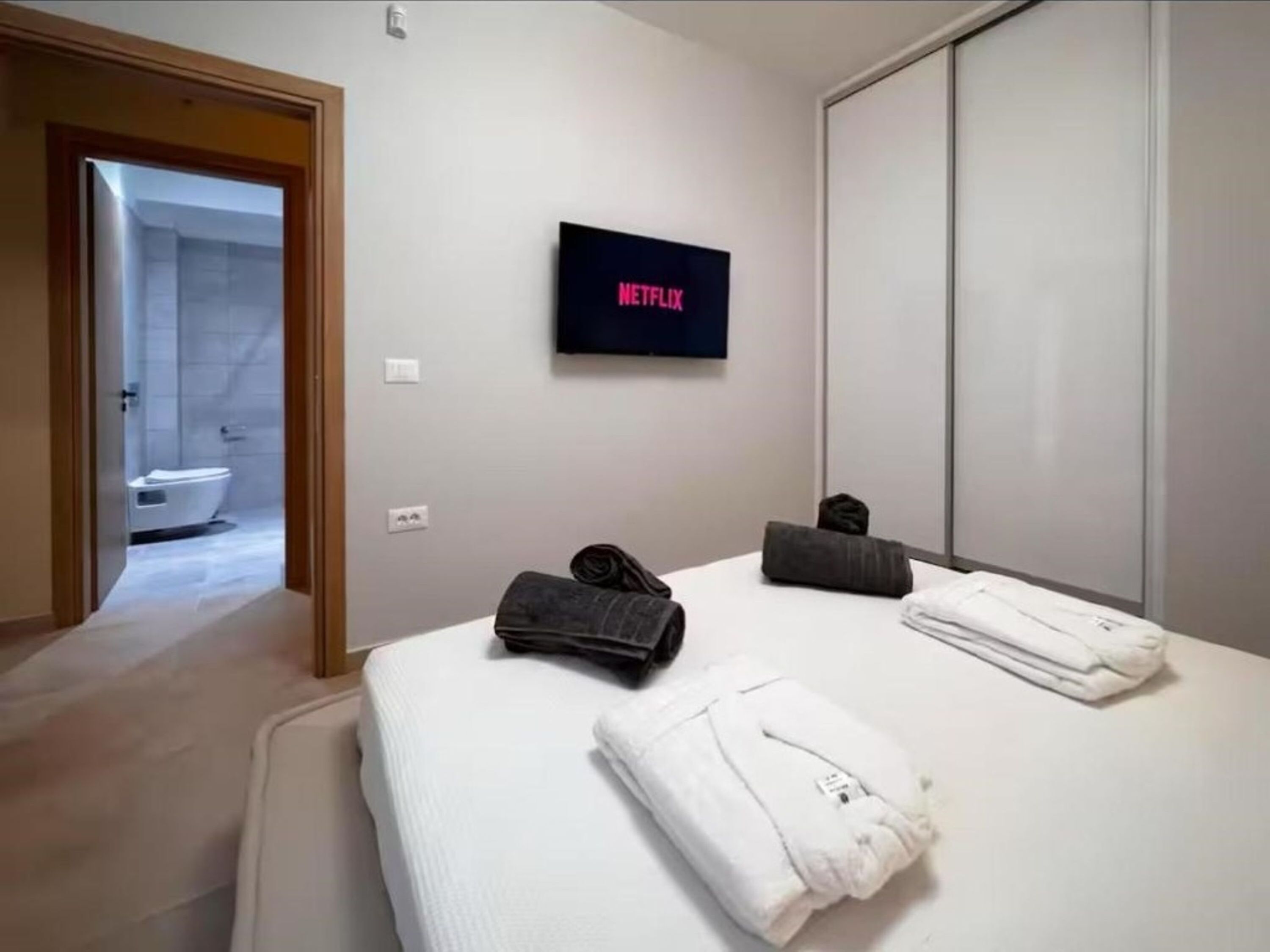 Hotellihuone, jossa on sänky, seinälle asennettu televisio, avoimesta ovesta näkyvä kylpyhuone ja vaatekaappi.