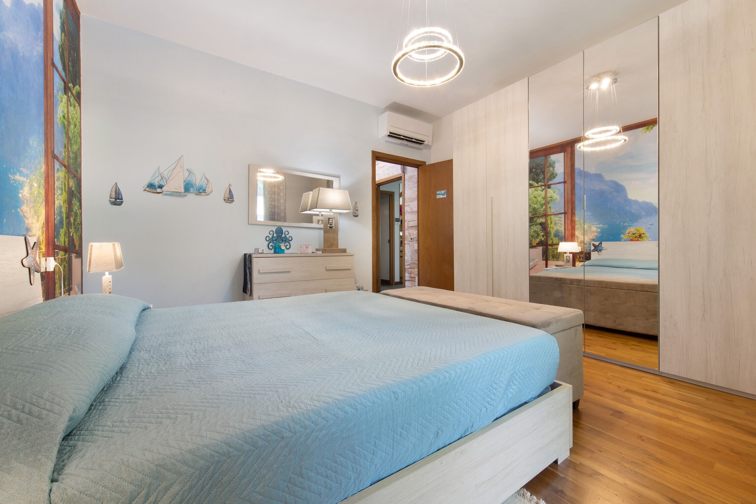A bedroom with a bed, a dresser, a mirror, and a view of the sea.