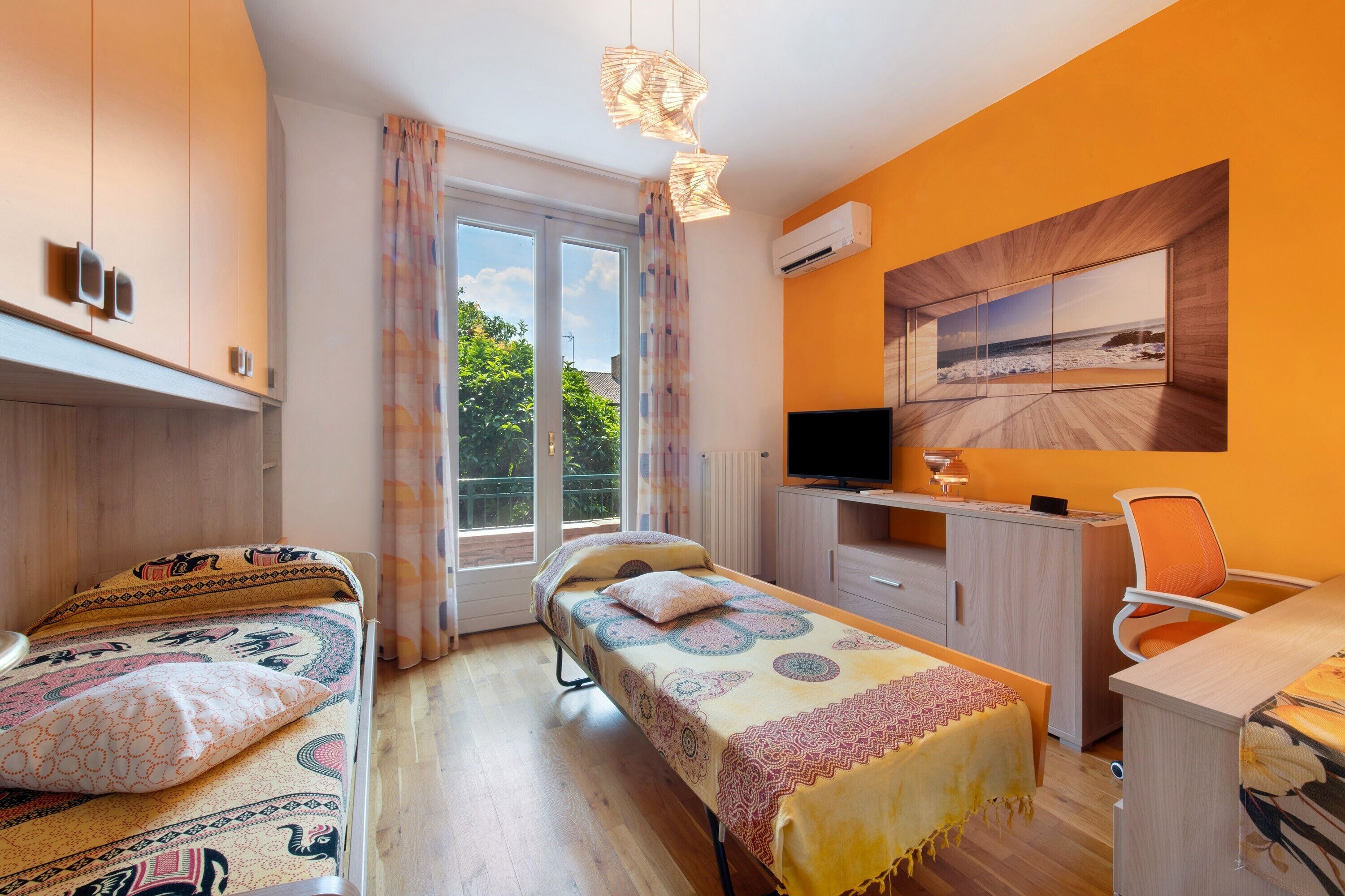 A bedroom with a bed, a desk, a chair, a TV, and a window with a view.