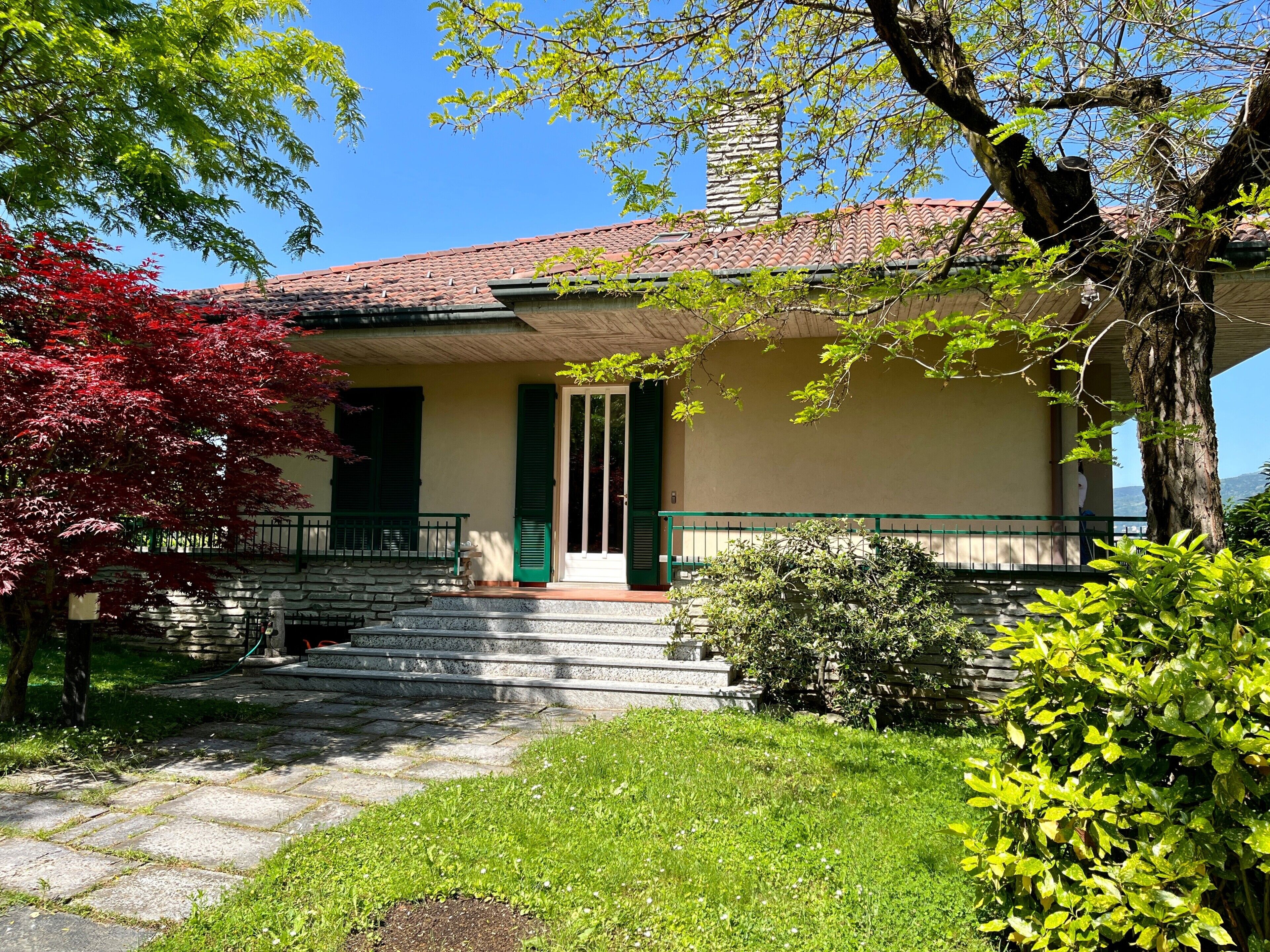 Un edificio con una scala in pietra che conduce a una porta verde, immerso nel verde e sotto un cielo azzurro intenso.