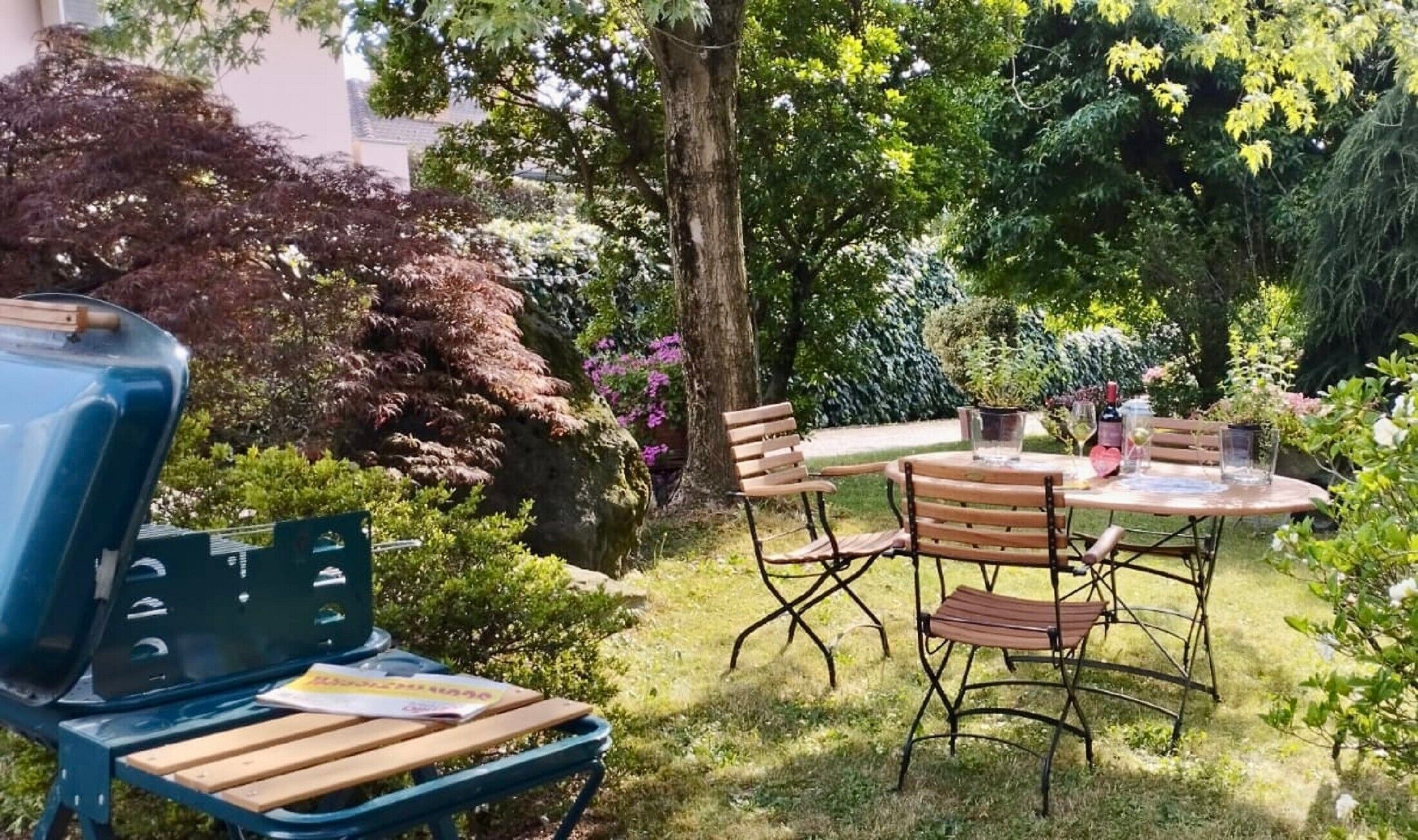 Eine Terrasse mit rundem Tisch und Stühlen, einem Grill und einer Bank.
