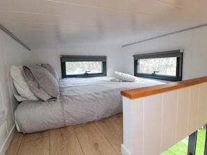 A bedroom with a bed, two windows, and a wooden floor. - The Tiny Home (Yarm)