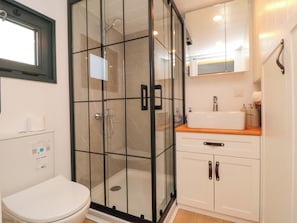 A bathroom with a glass-enclosed shower, a toilet, and a sink with a wooden countertop. - The Tiny Home (Yarm)