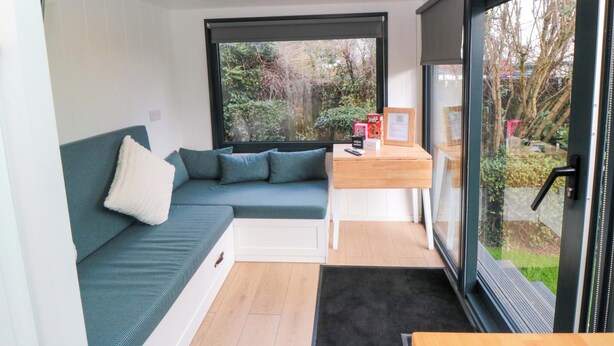 Ein modernes Zimmer mit einer Couch, einem kleinen Tisch und einem Fenster mit Blick auf Bäume.
