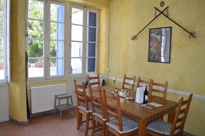 Un coin repas avec une table et des chaises en bois, une fenêtre avec des rideaux, un radiateur et un tableau accroché au mur.