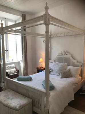 Un lit à baldaquin avec des poteaux aux quatre coins, un panneau de tête en bois et une table de chevet avec une lampe.