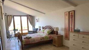 A bedroom with a bed, bedside tables, a dresser, a chair, and a window with curtains. - La Maison Tourouzelle (Lauraguel)