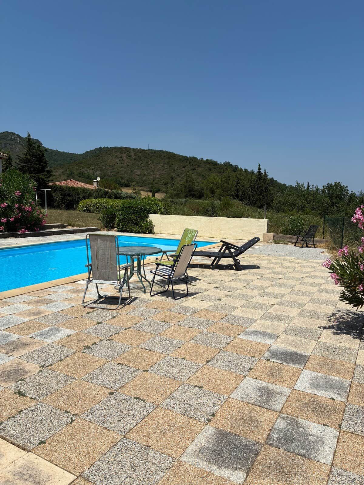 Un área de piscina con una mesa y sillas, rodeada por un patio empedrado.