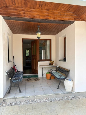 A covered porch with a wooden ceiling, a bench, a table, a potted plant, and a door leading inside. - La Maison de la lavande (Quillan)