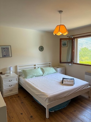 A bedroom with a bed, bedside tables, a hanging lamp, a clock, a window with a view, and a framed picture on the wall. - La Maison de la lavande (Quillan)
