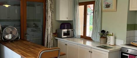 A kitchen with a wooden counter, white cabinets, a fan, a microwave, and a stove.