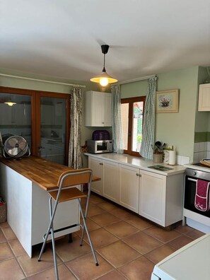 A kitchen with a wooden counter, white cabinets, a fan, a microwave, and a stove. - La Maison de la lavande (Quillan)