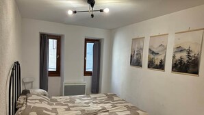 Un dormitorio con una cama, dos ventanas, un radiador y tres cuadros en la pared.