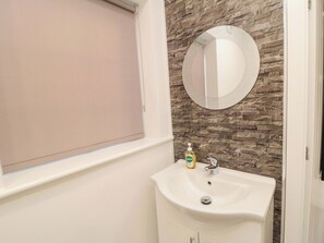 Een badkamer met een wit wastafel, een spiegel en een raam met een beige jaloezie.