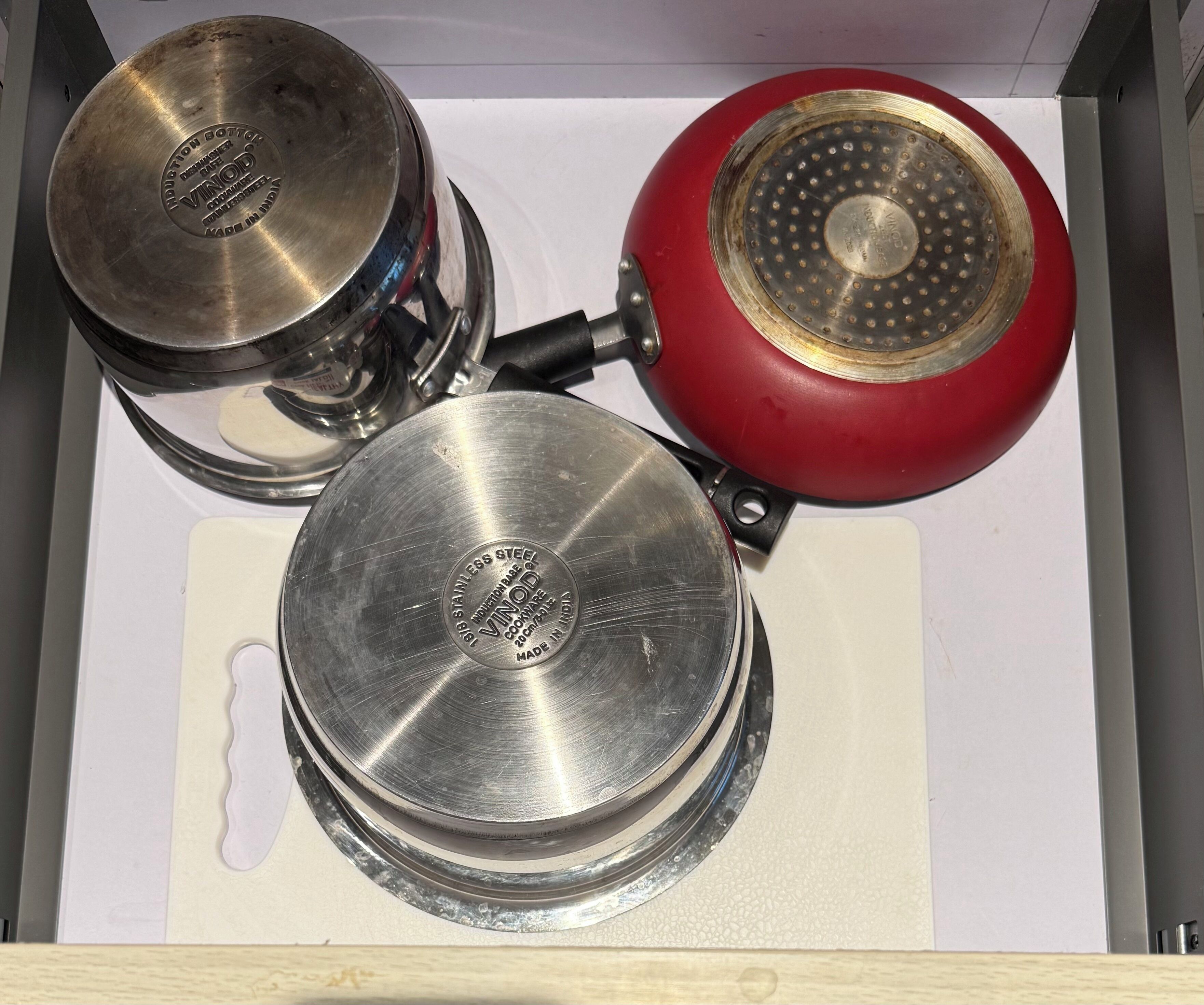 A drawer containing stainless steel cookware with a red pan.