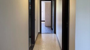 En gang med lysegrå gulv, hvide vægge og en loftlampe.