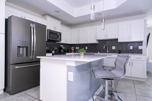 Een moderne keuken met een roestvrijstalen koelkast, een magnetron, een spoelbak en een barkruk.