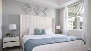 Ein Schlafzimmer mit einem großen Bett, zwei Nachttischen, einem Fenster mit Jalousien und Wanddekoration.