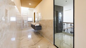 Un baño moderno con piso de mármol, lavamanos suspendido y zona de ducha con mampara de vidrio.