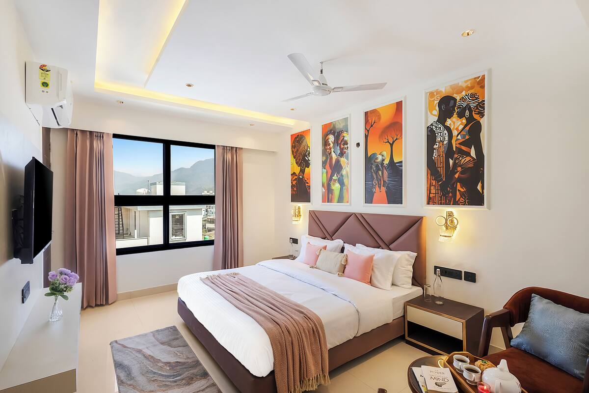 Un hotel moderno con una cama grande, televisor de pantalla plana, ventilador de techo, obras de arte en las paredes y una ventana con vistas a la ciudad.