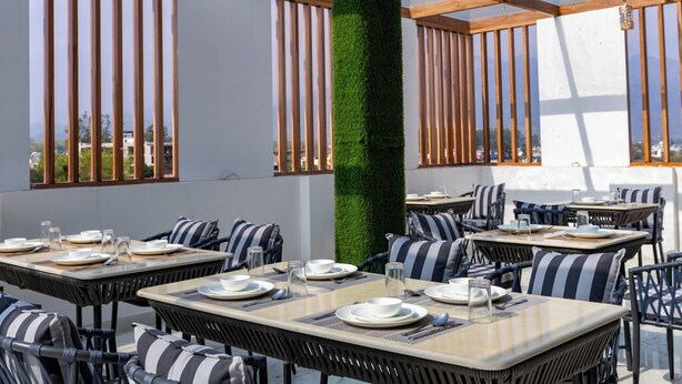 Un área de comedor al aire libre con mesas y sillas, una columna central y vistas a la ciudad.