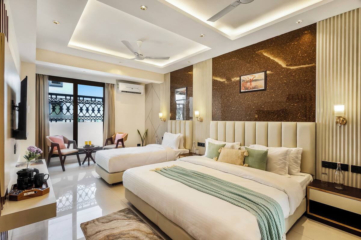 Habitación de hotel con dos camas, televisor, escritorio con silla, balcón y ventilador de techo.
