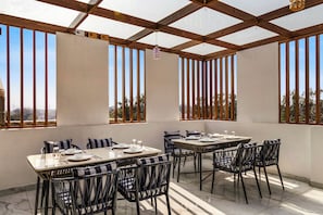 A covered outdoor dining area with tables and chairs, large windows, and a view of the landscape. - Anandam in the Himalyas By Alaya Stays (Rishikesh)