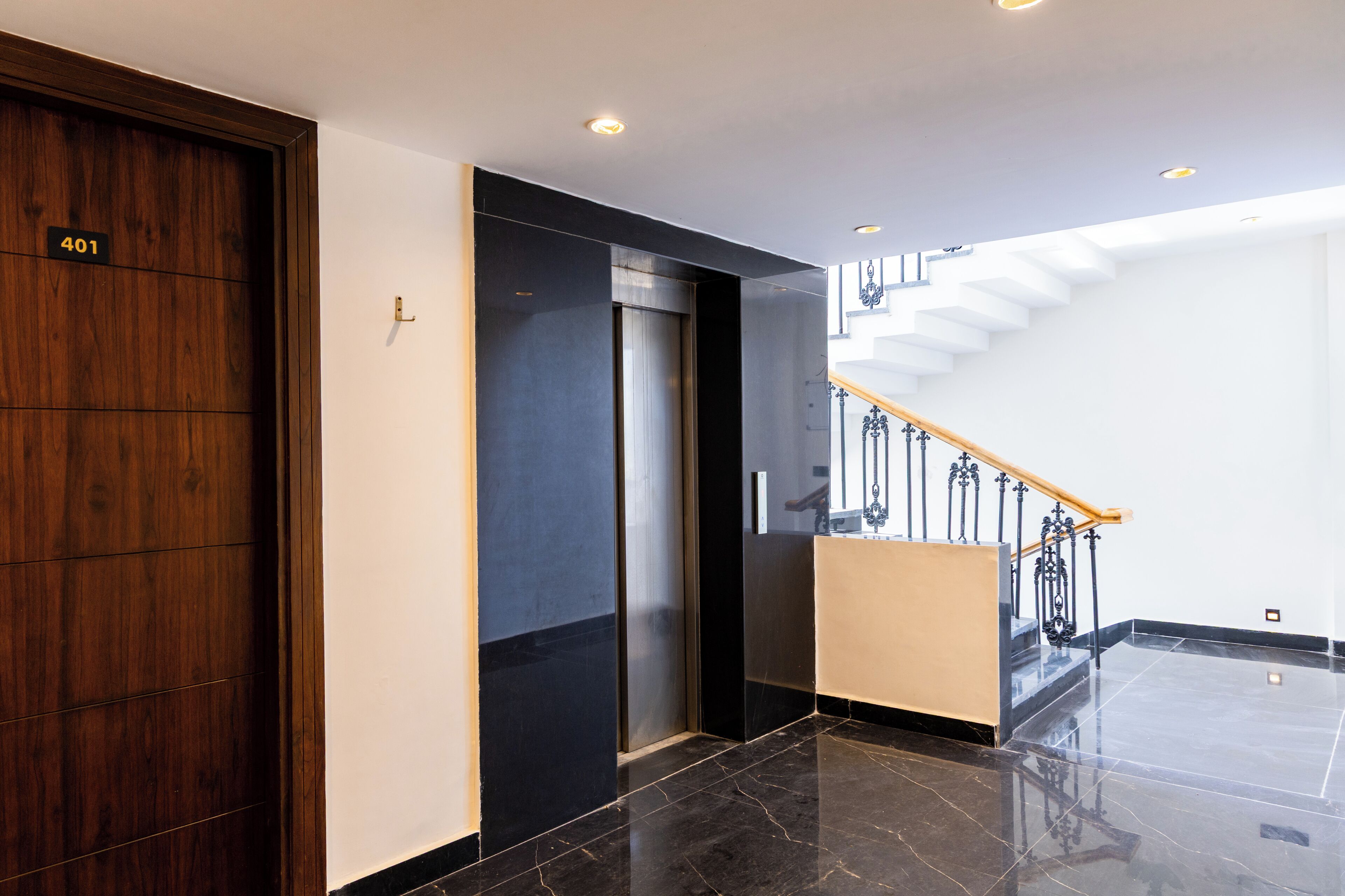 A modern interior with a wooden door marked '401', a black elevator, and a staircase with a wooden handrail.