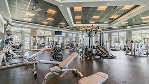Ein Fitnessstudio mit verschiedenen Trainingsgeräten, großen Fenstern und hoher Decke.