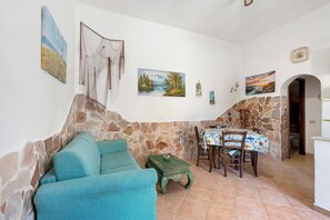 Un salon avec un mur en pierre, un canapé bleu, une table à manger avec des chaises et diverses œuvres d’art accrochées au mur.