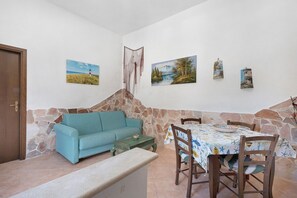 Quarto com parede de pedra, sofá azul, mesa de jantar com cadeiras e quadros nas paredes.