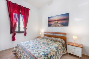 Quarto com cama, duas mesas de cabeceira, um criado-mudo, janela com cortinas e um quadro pendurado na parede.