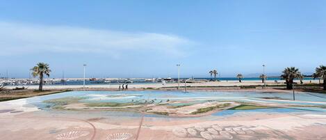Zona de playa con un mural grande, palmeras y cielo despejado.