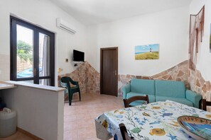 Quarto com sofá, mesa de jantar, televisão e porta.