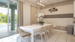 Un coin repas avec une table dressée pour six personnes, une orchidée en pot et un élément décoratif fixé au mur.